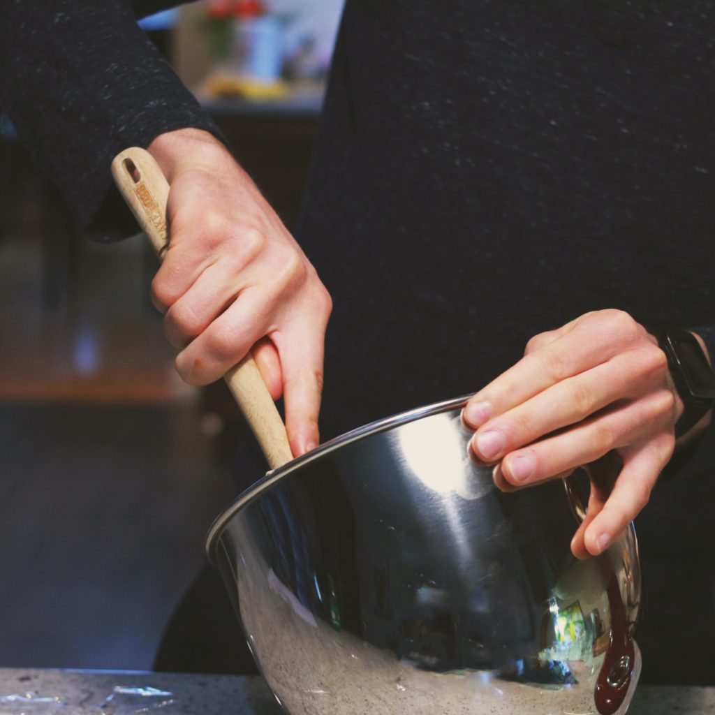 Person in black sweatshirt mixing kratom strains in a metal mixing bowl