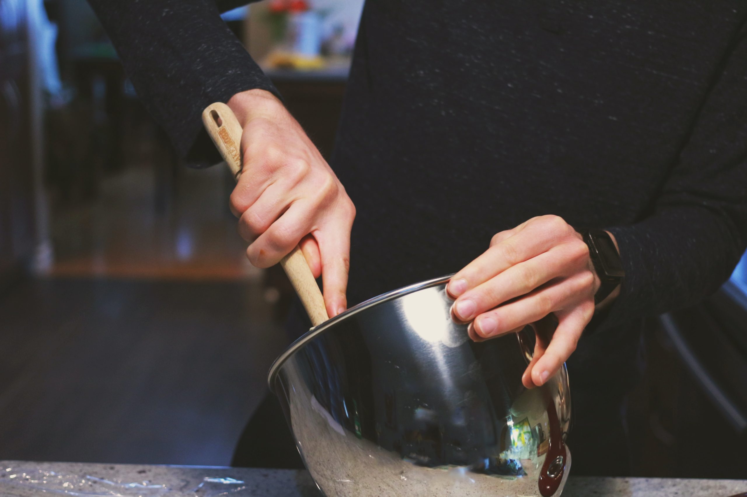 Person in black sweatshirt mixing kratom strains in a metal mixing bowl